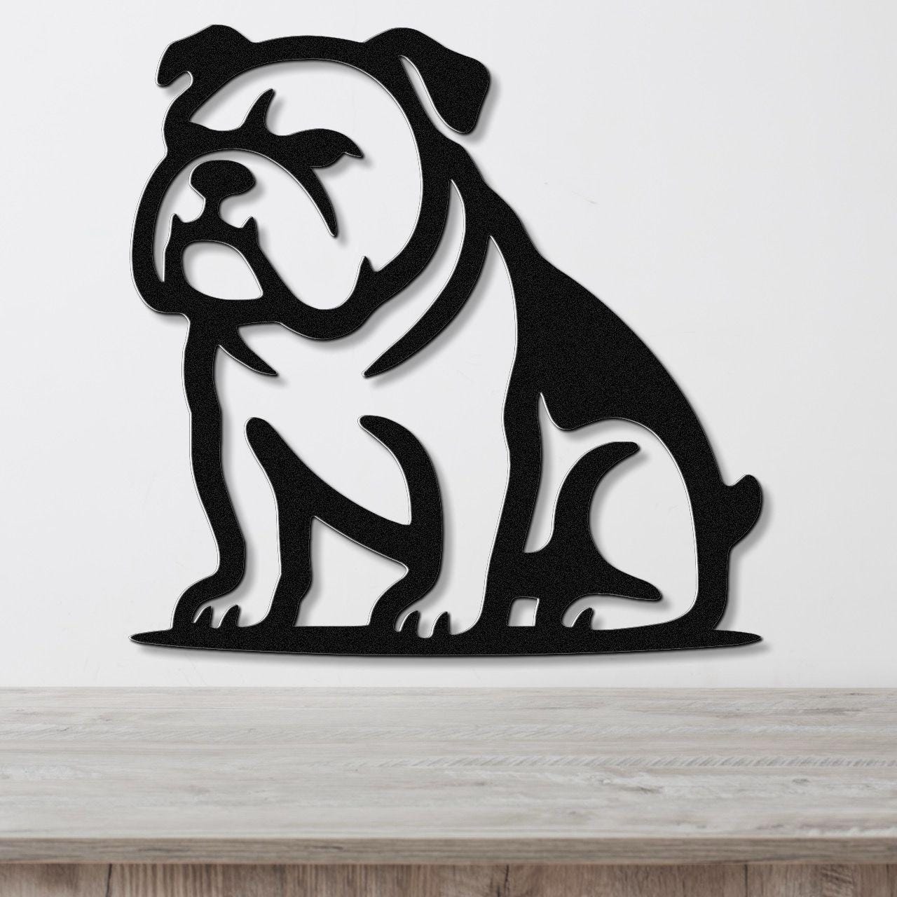 Black metal bulldog wall art with a bold silhouette and internal cutouts, mounted on a white wall above a wooden surface.