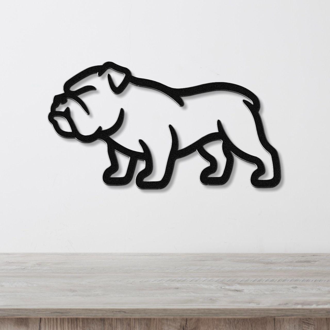 Black metal bulldog wall art silhouette with cutout details, mounted on a white wall above a light wood surface.