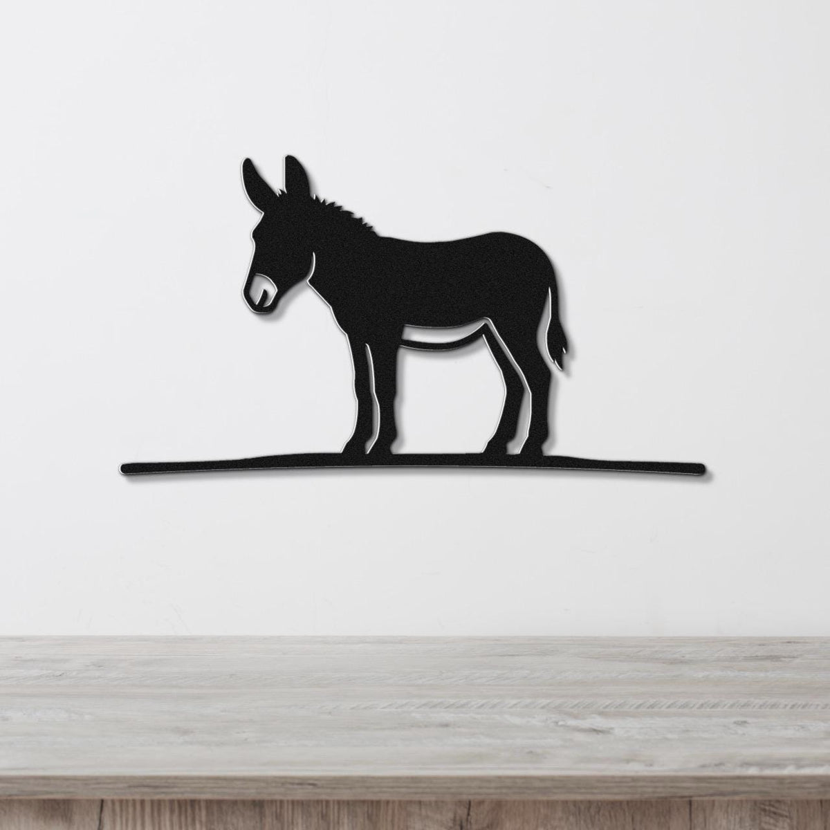 Black metal donkey wall art silhouette with a long horizontal base, mounted on a white wall above a wooden surface.