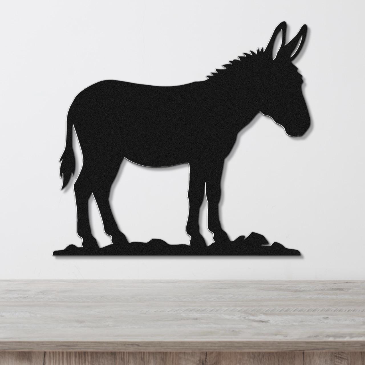 Black metal donkey silhouette wall art with a textured mane and tail, mounted on a white wall above a light wood surface.