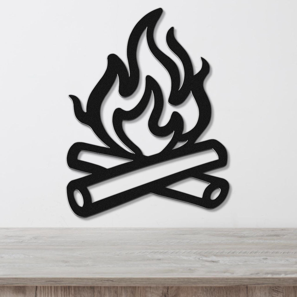 Black metal campfire wall art with flame and log cutouts, mounted on a white wall above a wooden surface.