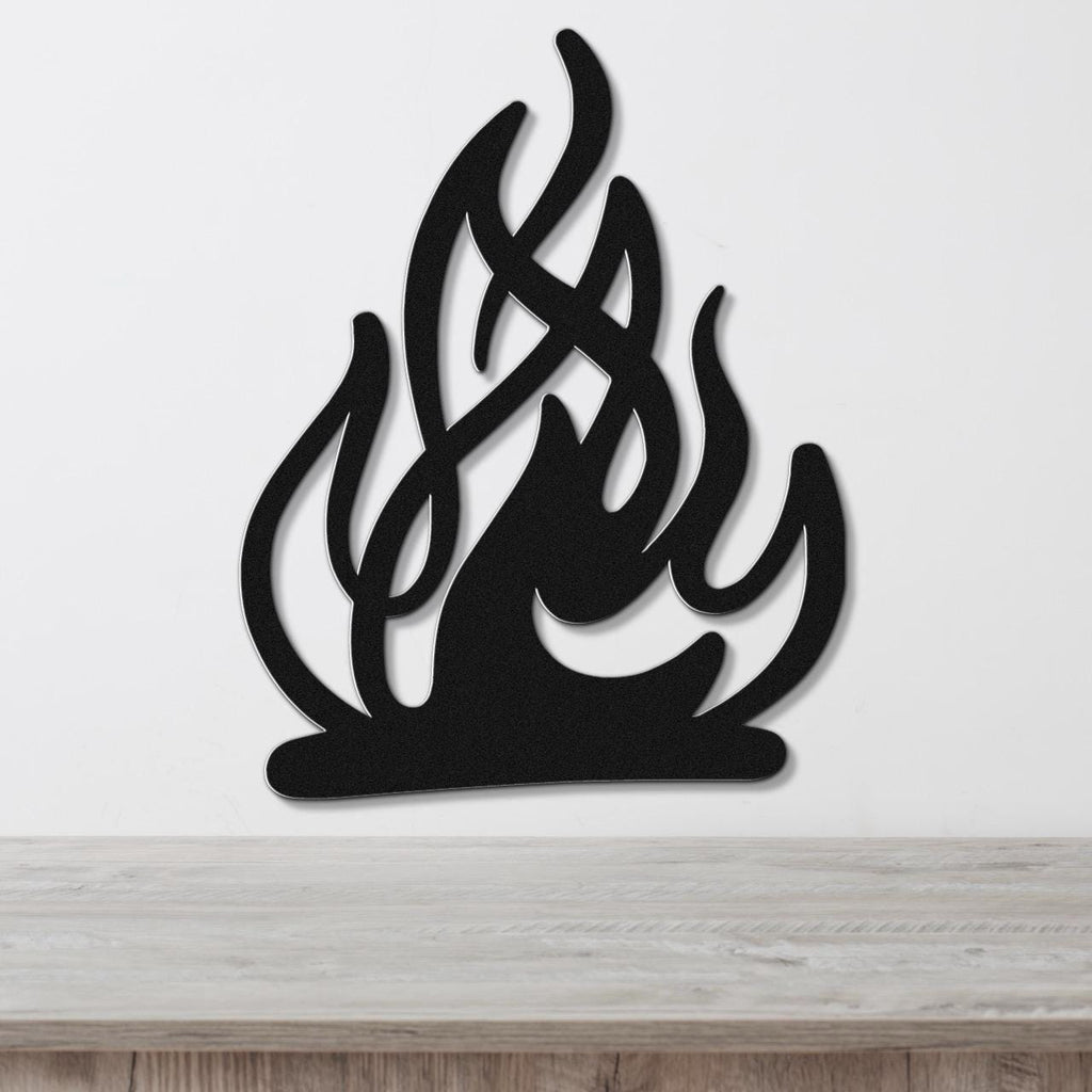 Black metal wall art in a flame silhouette design with internal cutout details, mounted on a white wall above a light wood surface.