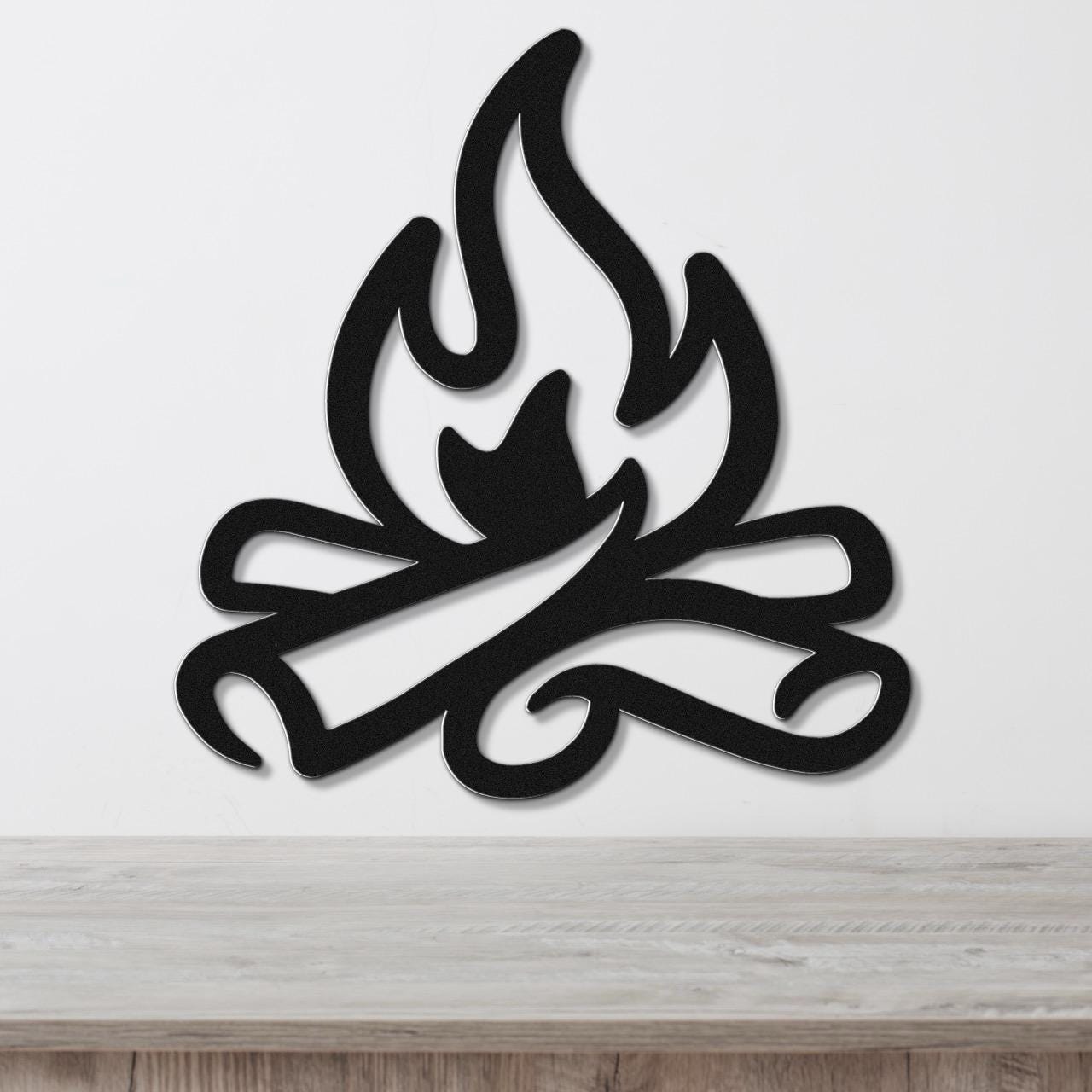 Black metal wall art in a flame and log silhouette design, mounted on a white wall above a light wood surface.