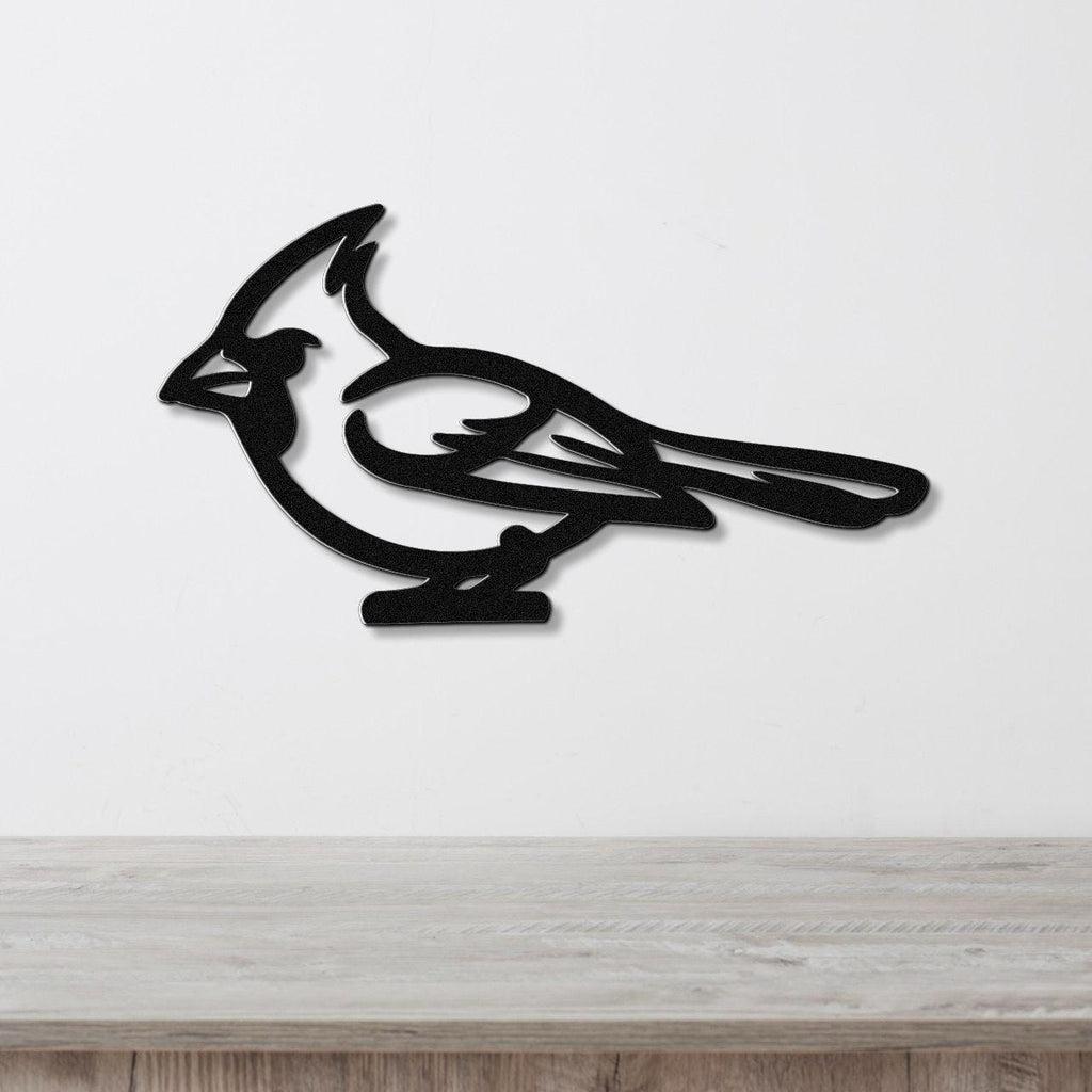 Black metal cardinal wall art with a bold silhouette and internal cutout details, mounted on a white wall above a light wood countertop.