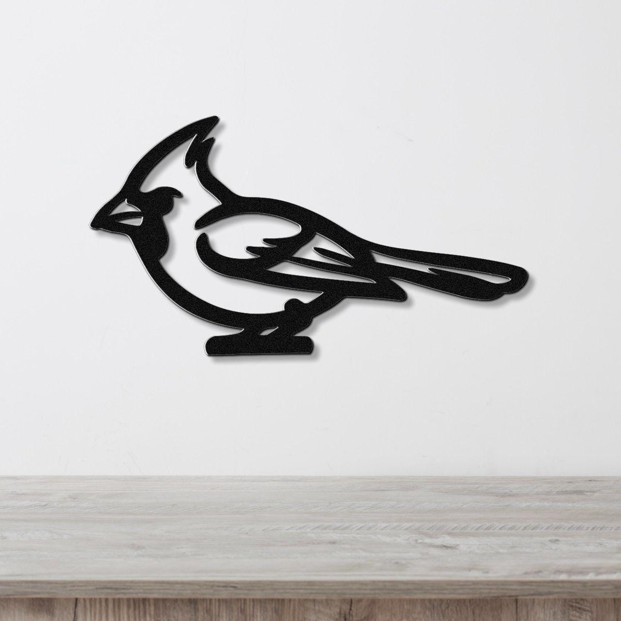 Black metal cardinal wall art with a bold silhouette and internal cutout details, mounted on a white wall above a light wood countertop.