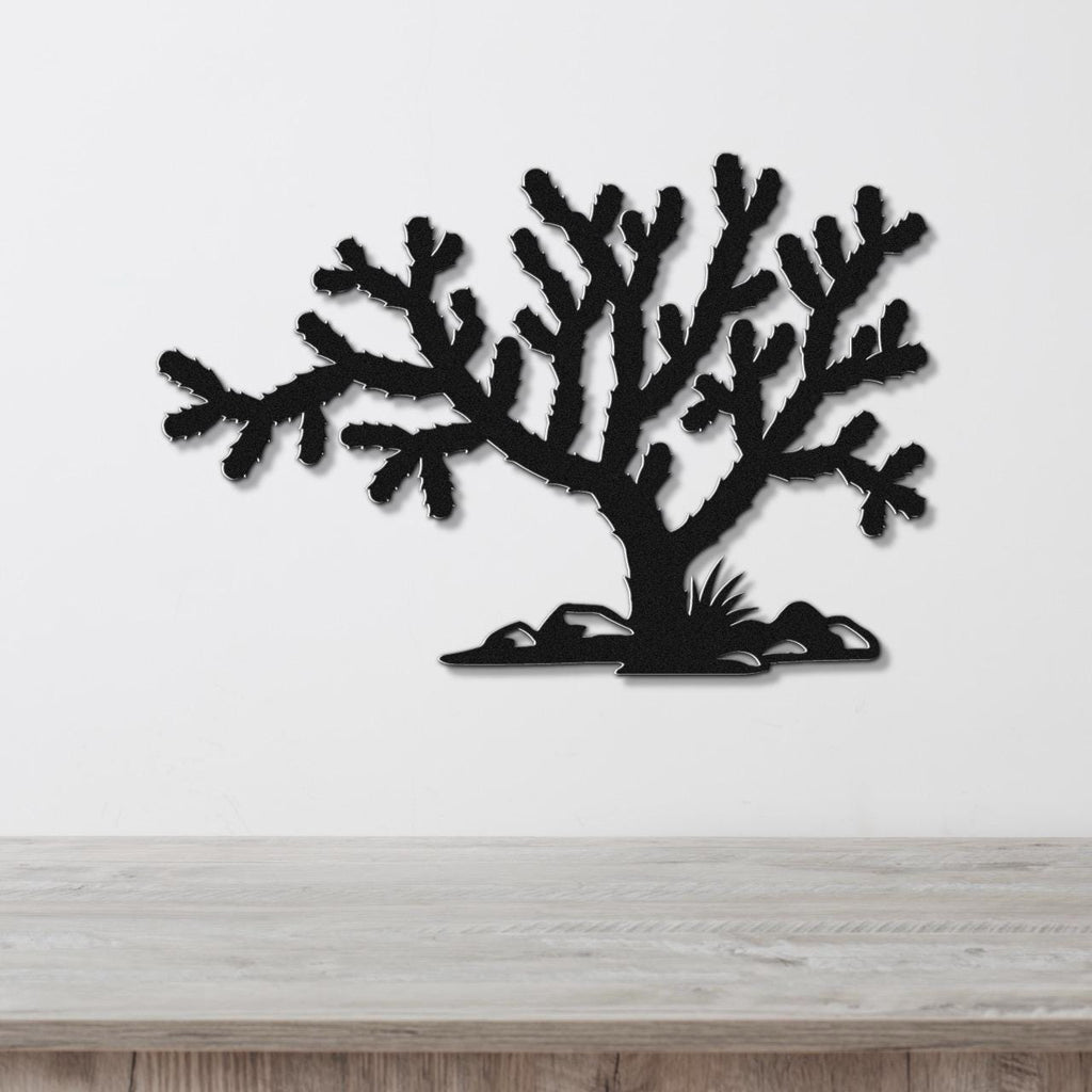 Black metal wall art cutout of a cholla cactus with branching arms and base detail, mounted on a white wall above a light wood surface.