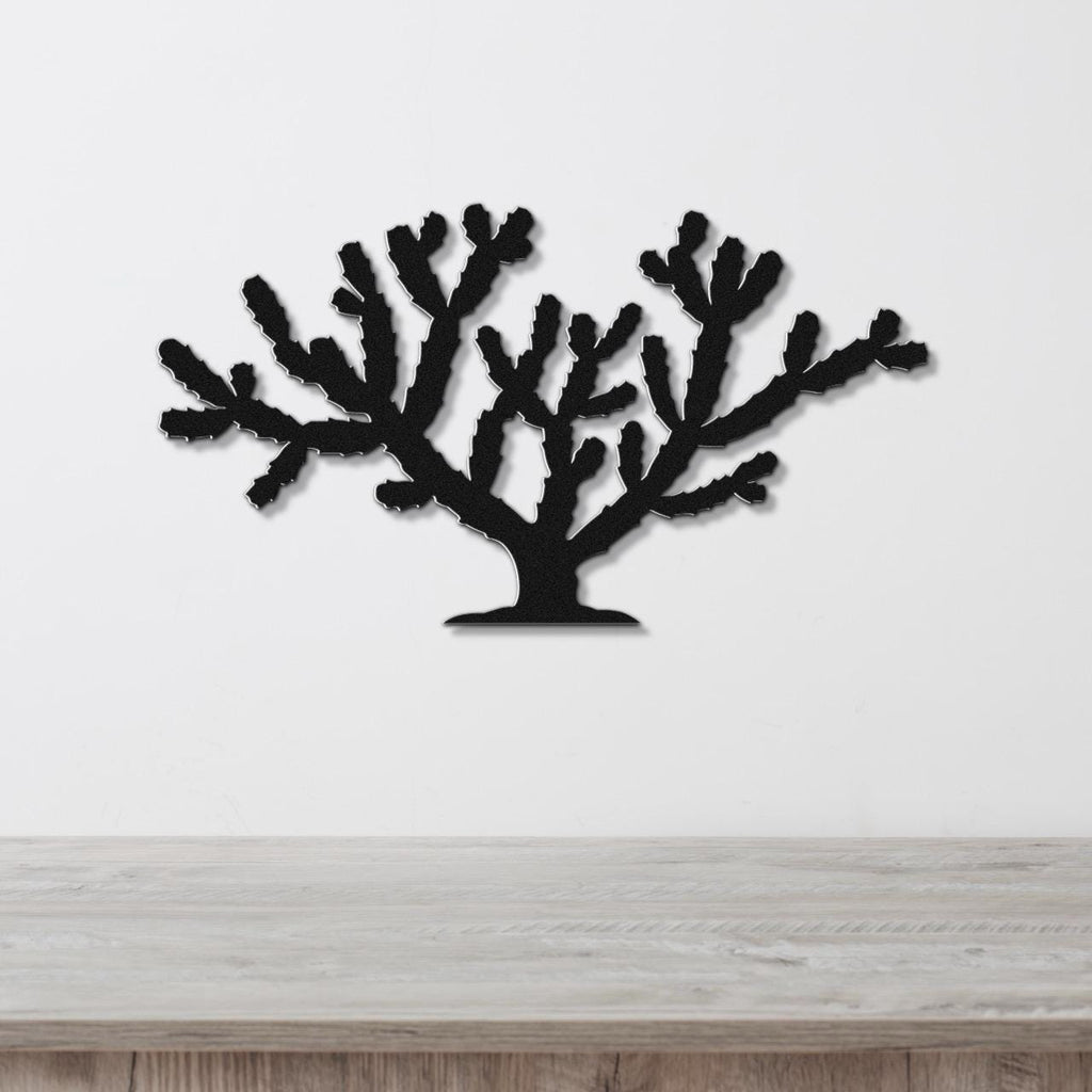 Black metal wall art cutout of a cholla cactus with branching arms, mounted on a white wall above a light wood surface.