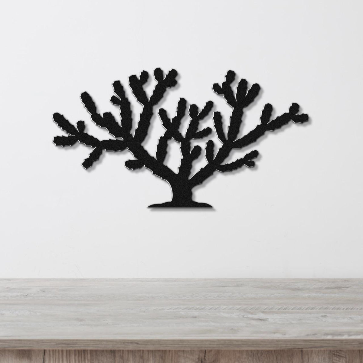 Black metal wall art cutout of a cholla cactus with branching arms, mounted on a white wall above a light wood surface.