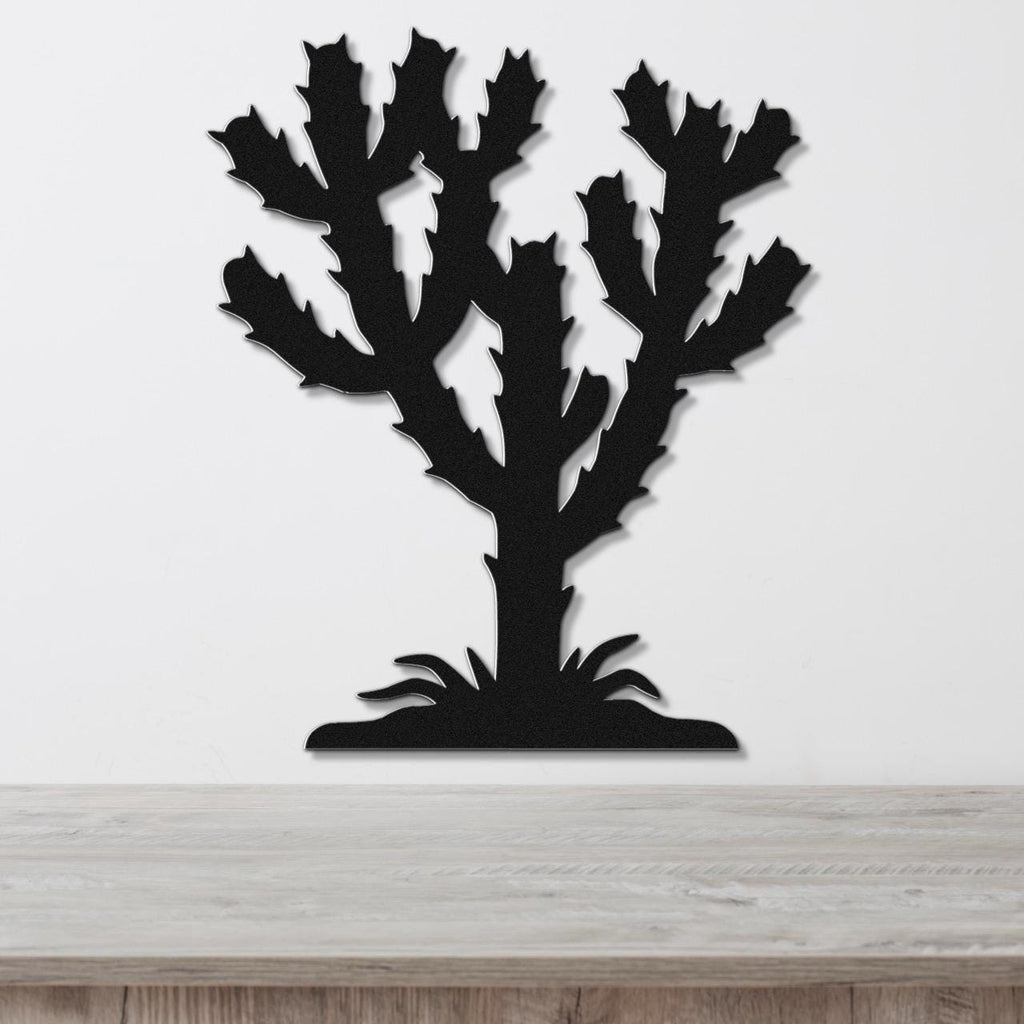 Black metal wall art cutout of a cholla cactus with branching arms and spines, mounted on a white wall above a light wood surface.