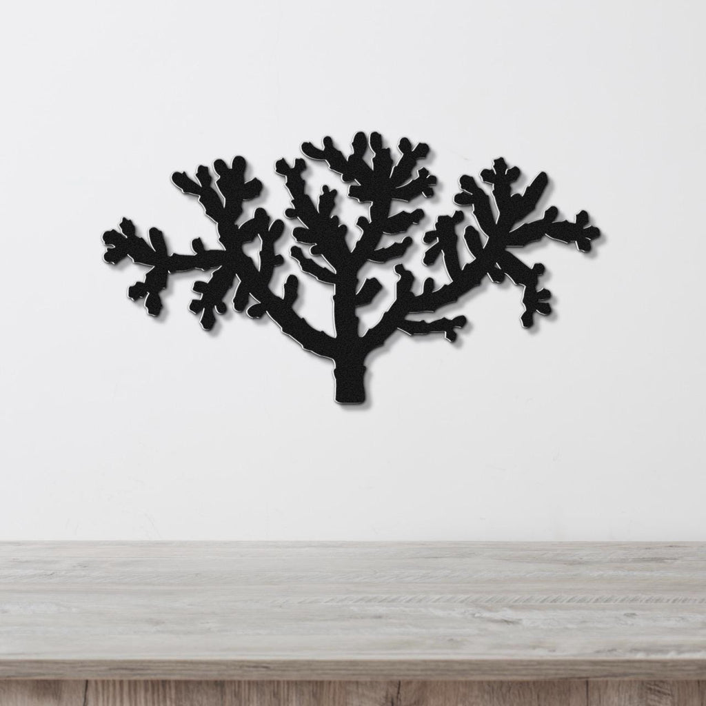 Black metal wall art cutout of a cholla cactus with branching arms, mounted on a white wall above a light wood surface.