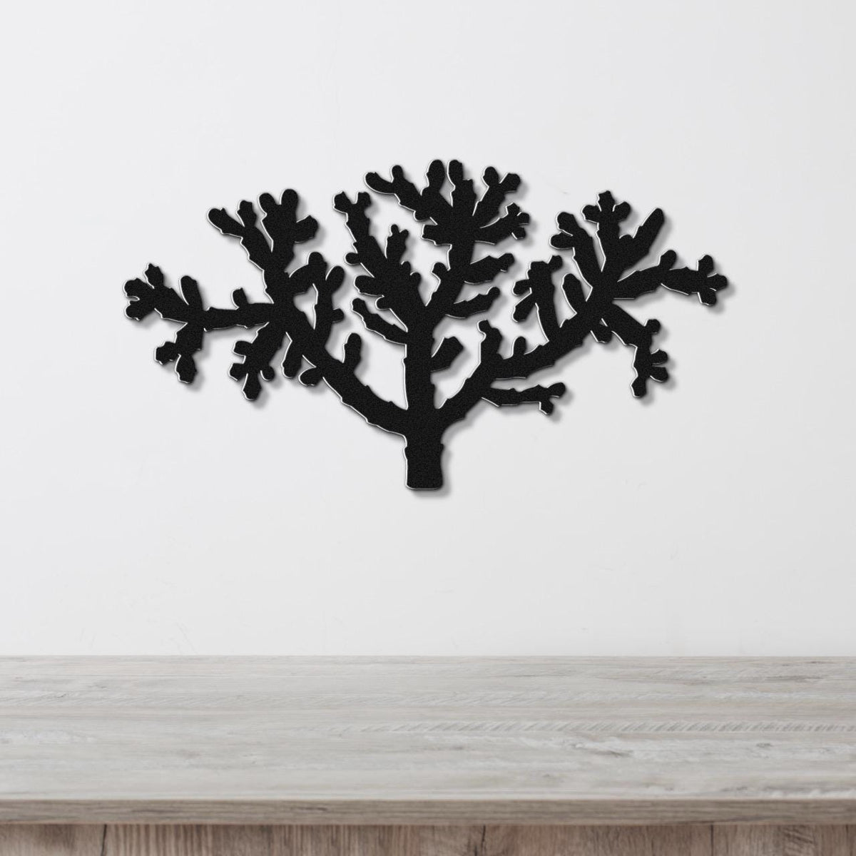 Black metal wall art cutout of a cholla cactus with branching arms, mounted on a white wall above a light wood surface.