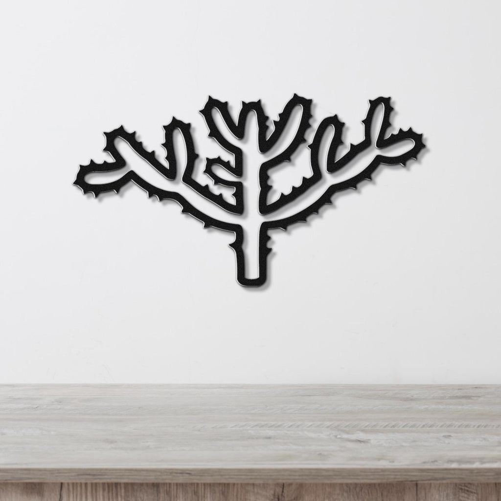 Black metal wall art cutout of a cholla cactus with spiny branches, mounted on a white wall above a light wood surface.