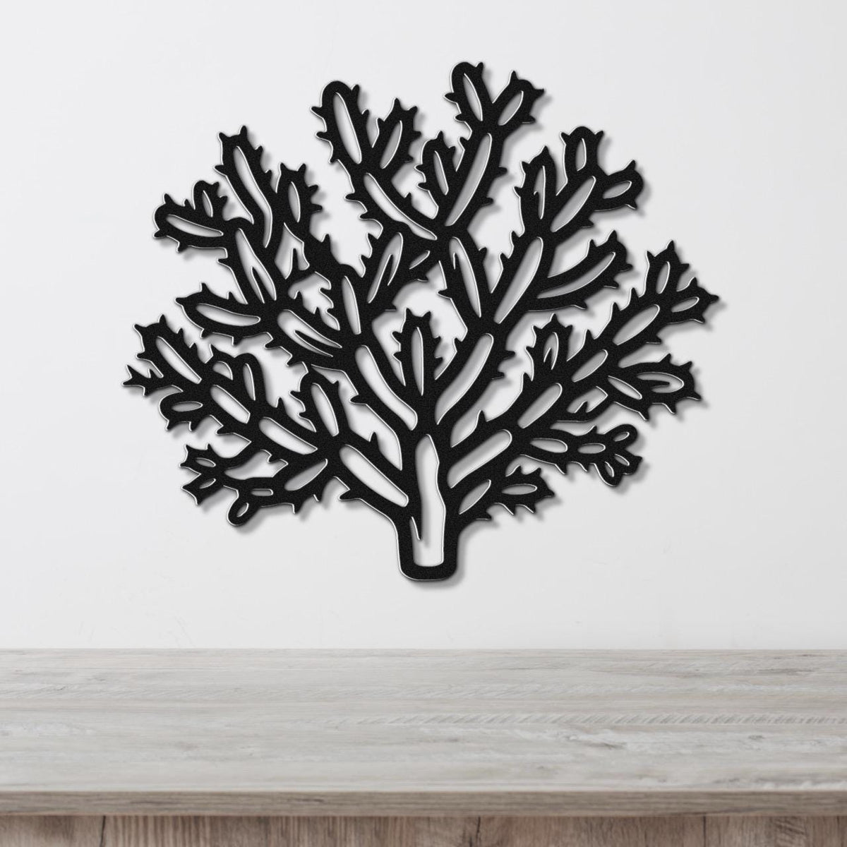 Black metal wall art cutout of a cholla cactus with branching arms and spines, mounted on a white wall above a light wood surface.