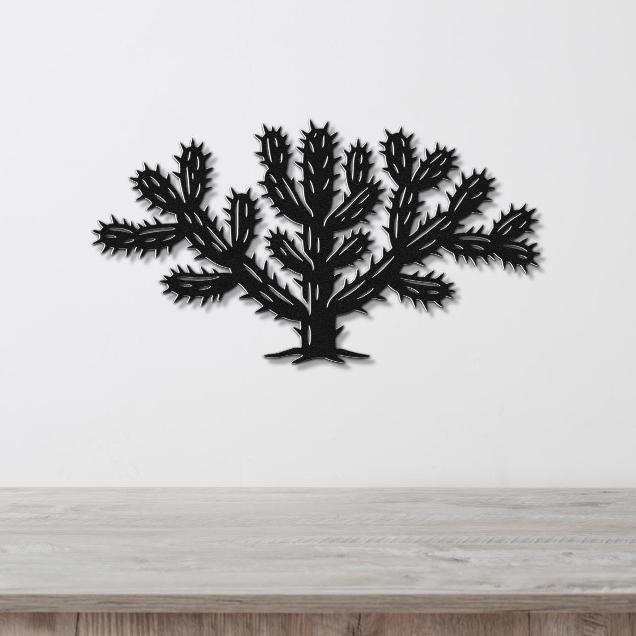 Black metal Cholla cactus wall art with detailed spines and branching cutouts, mounted on a white wall above a light wood counter.