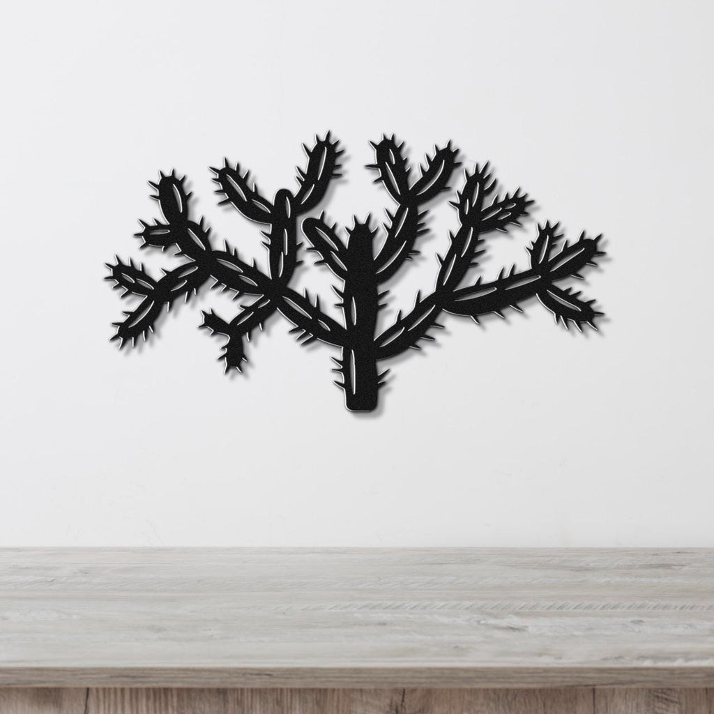 Black metal wall art cutout of a cholla cactus with textured spine details, mounted on a white wall above a light wood surface.
