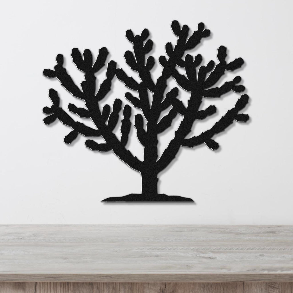 Black metal wall art silhouette of a cholla cactus with branching arms, mounted on a white wall above a light wood surface.