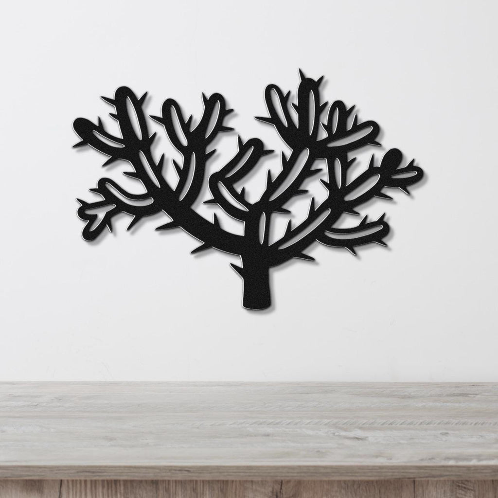 Black metal wall art cutout of a cholla cactus with branching arms and spines, mounted on a white wall above a light wood surface.
