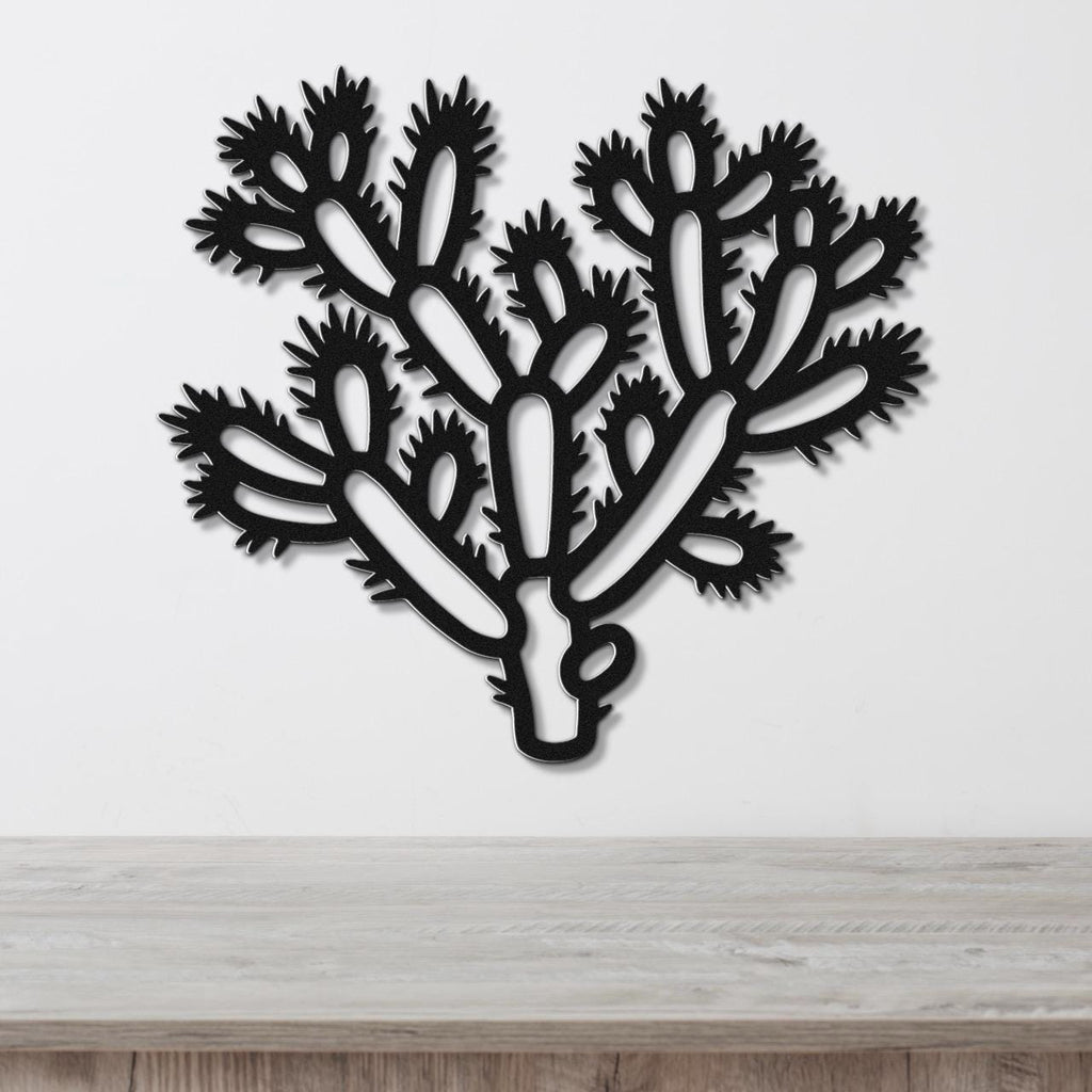 Black metal wall art cutout of a cholla cactus with spiny branches, mounted on a white wall above a light wood counter.