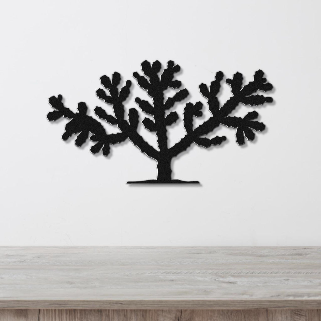 Black metal wall art silhouette of a cholla cactus with branching arms, mounted on a white wall above a light wood surface.