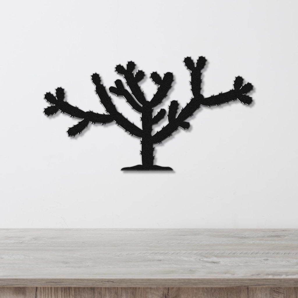 Black metal Cholla cactus wall art with spiky branch cutouts, mounted on a white wall above a light wood counter.