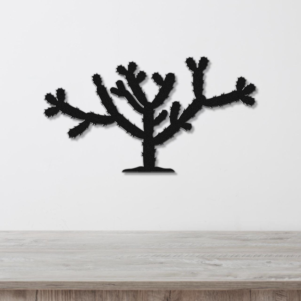 Black metal Cholla cactus wall art with spiky branch cutouts, mounted on a white wall above a light wood counter.
