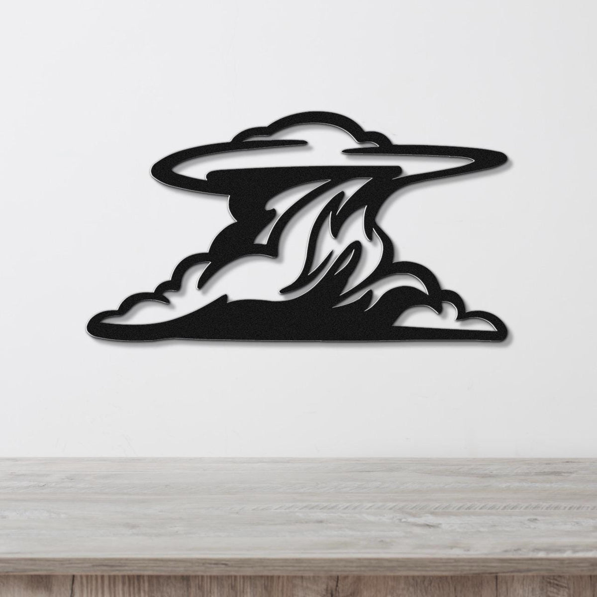 Black metal wall art in a cloud silhouette with internal flame-like cutouts, mounted on a white wall above a light wood surface.