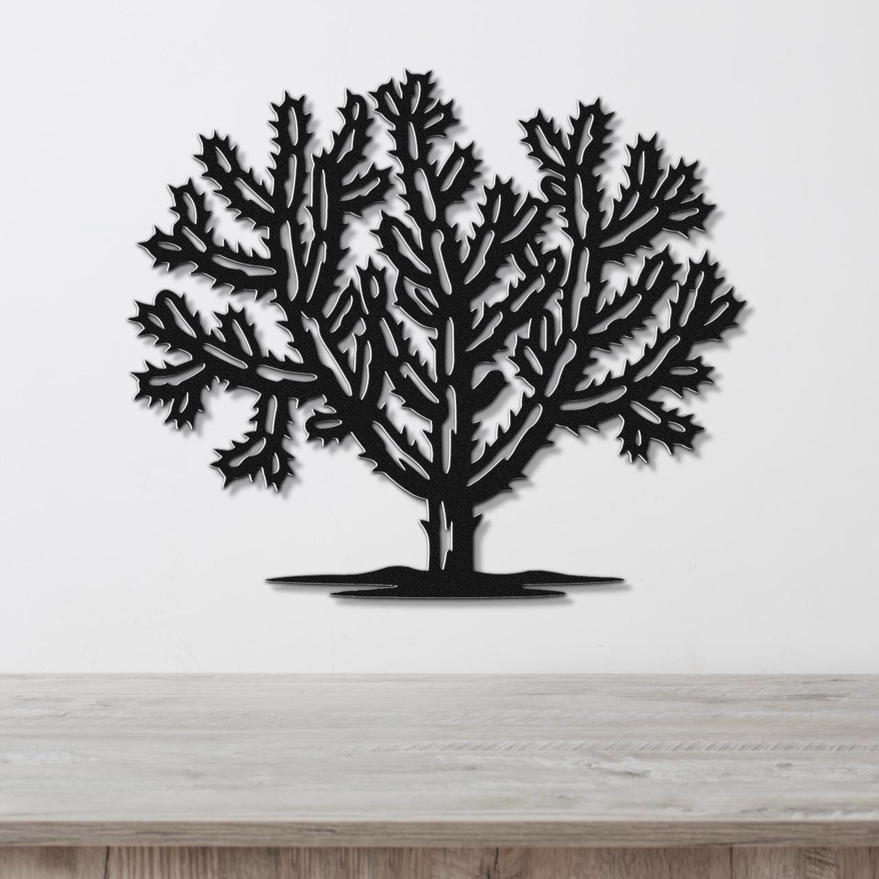 Black metal wall art cutout of a cholla cactus with intricate branching and spiny details, mounted on a white wall above a wooden surface.