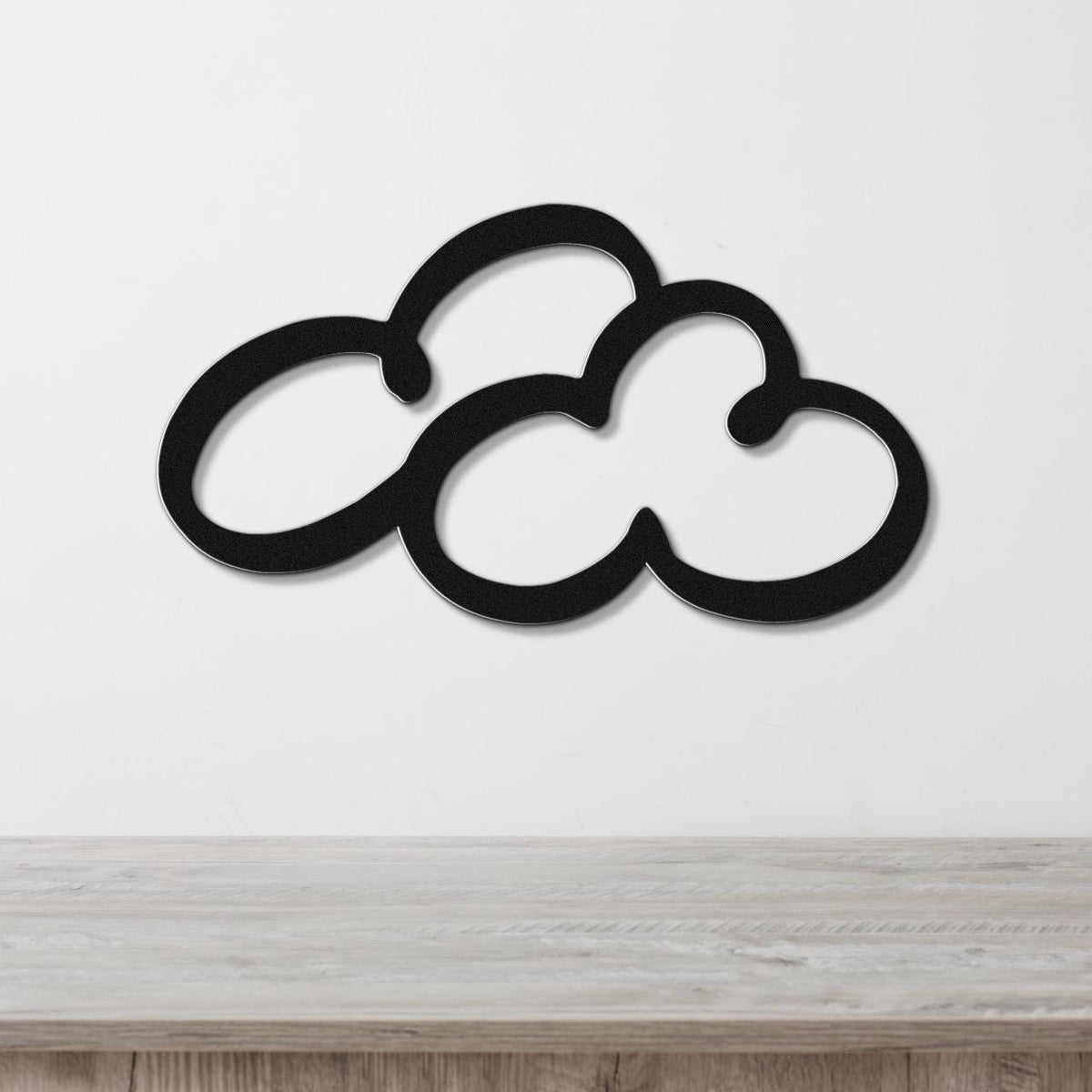 Black metal cloud-shaped wall art with cutout design, mounted on a white wall above a light wood surface.