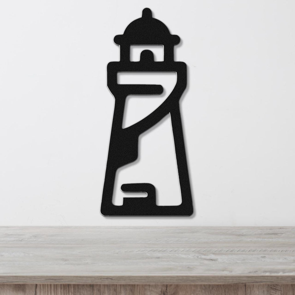 Black metal lighthouse wall art with cutout details, mounted on a white wall above a wooden surface.