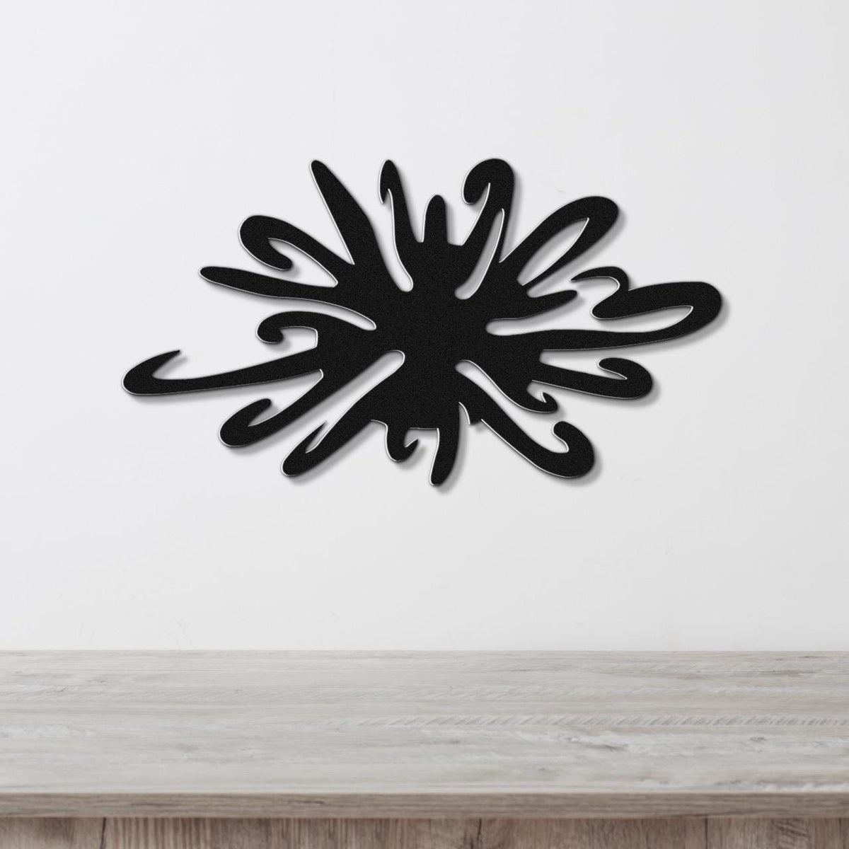 Black metal sea urchin wall art with organic spines and cutout details, mounted on a white wall above a wooden surface.