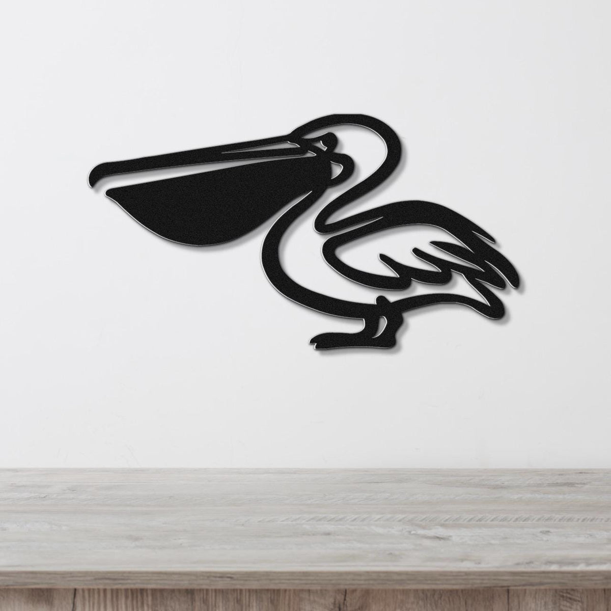 Black metal pelican wall art with a cutout silhouette design, mounted on a white wall above a light wood surface.