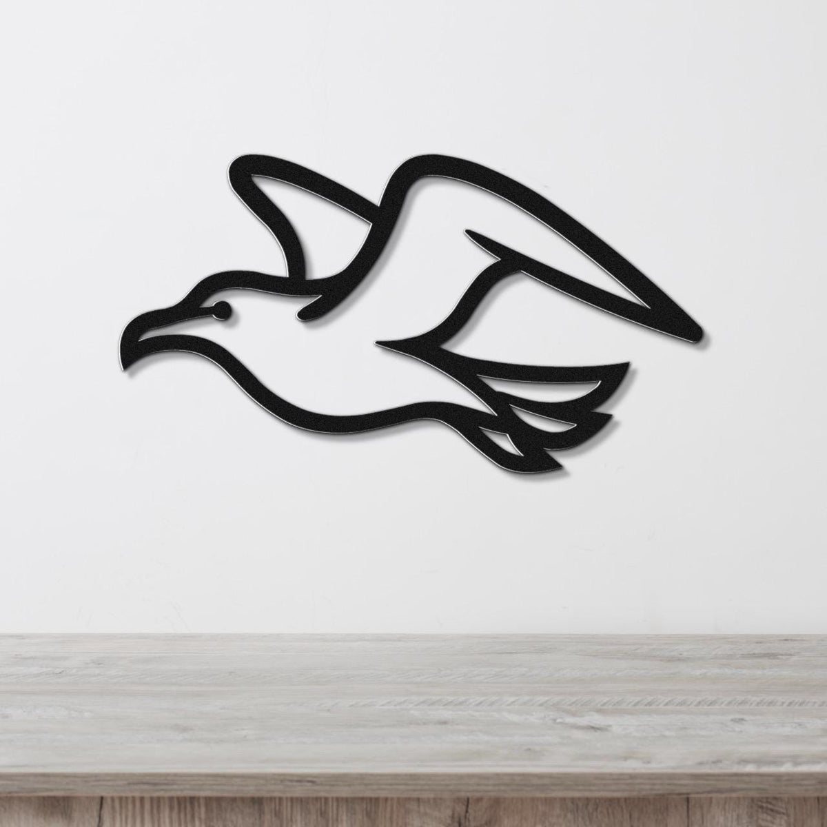 Black metal seagull wall art with wing and tail cutouts, mounted on a white wall above a light wood counter.