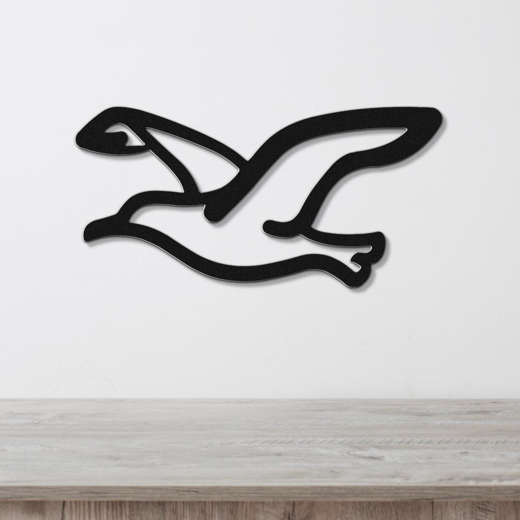 Black metal seagull wall art with a cutout silhouette design, mounted on a white wall above a light wood surface.