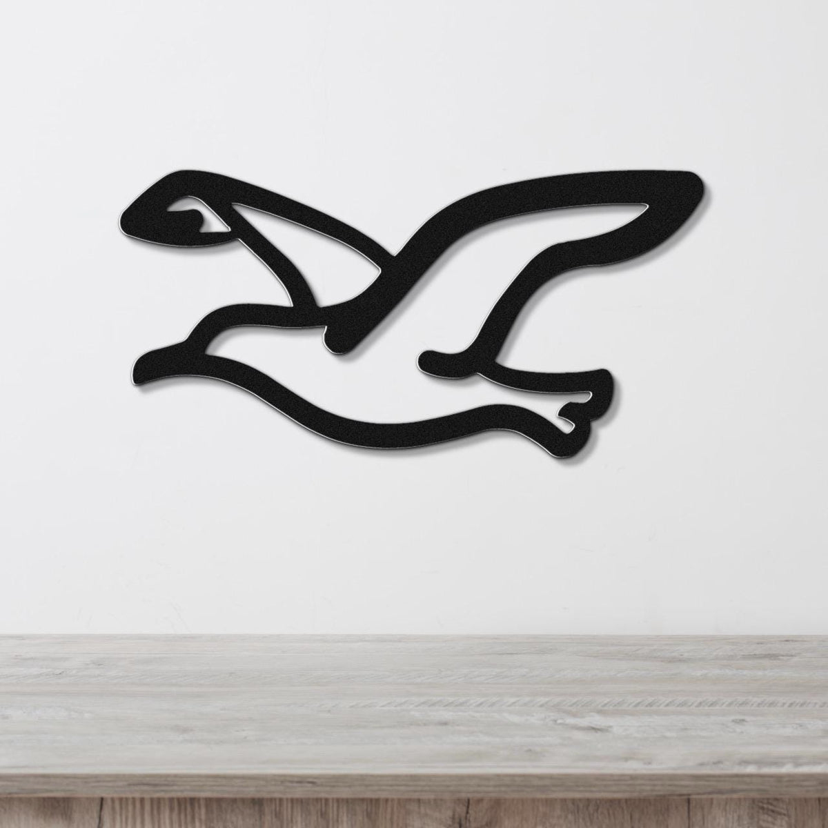 Black metal seagull wall art with a cutout silhouette design, mounted on a white wall above a light wood surface.