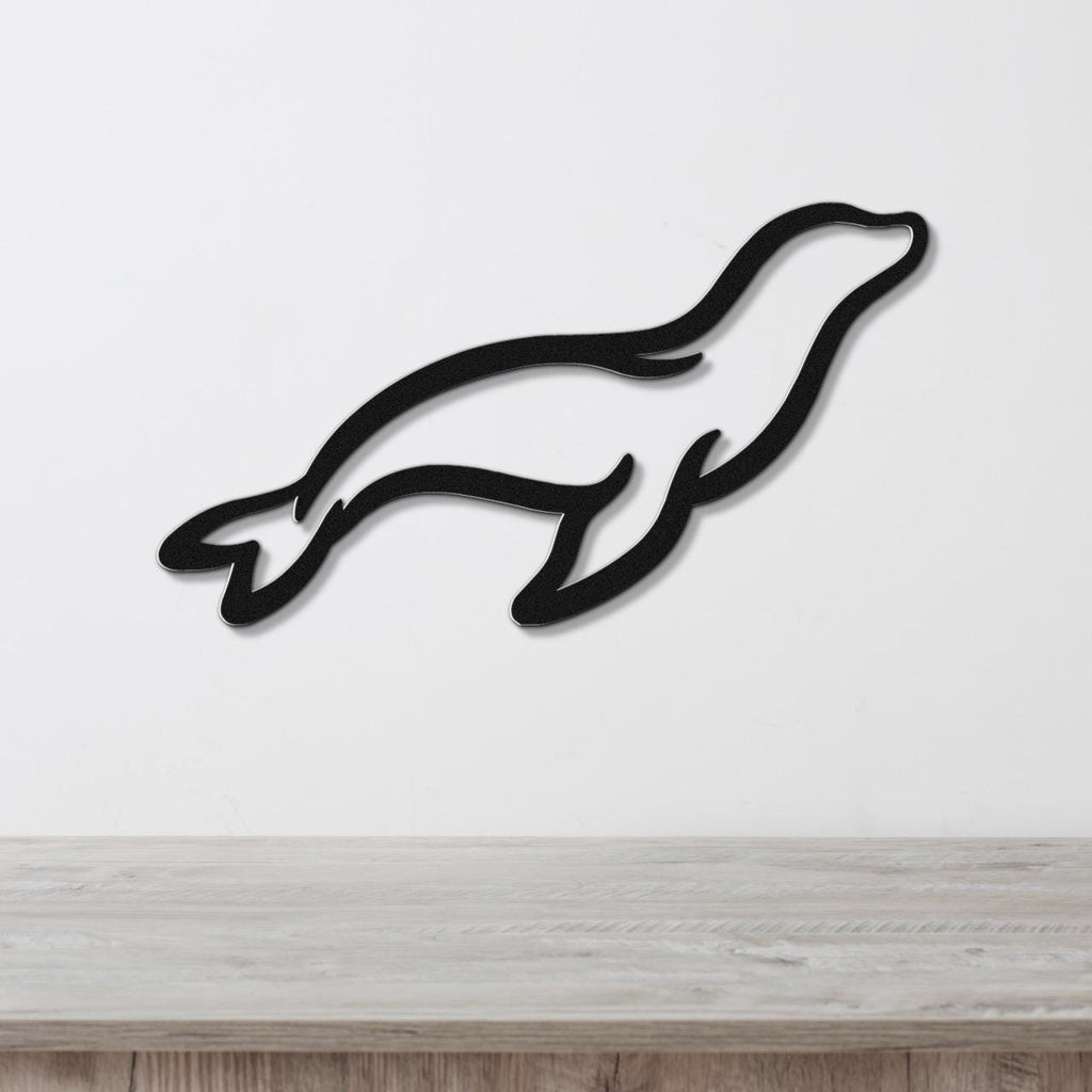Black metal sea lion wall art with a sleek silhouette design, mounted on a white wall above a light wood surface.