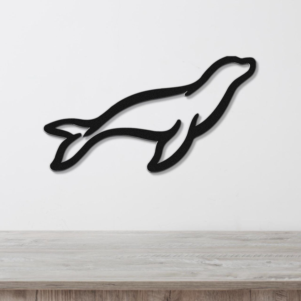 Black metal sea lion wall art silhouette with internal cutout details, mounted on a white wall above a light wood surface.