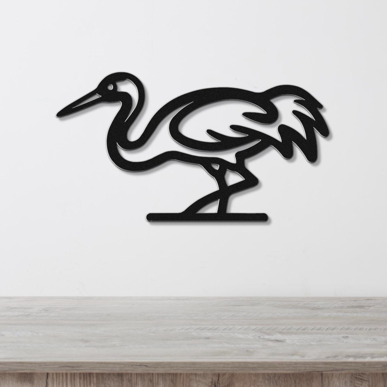 Black metal crane wall art with a cutout silhouette design, mounted on a white wall above a light wood surface.