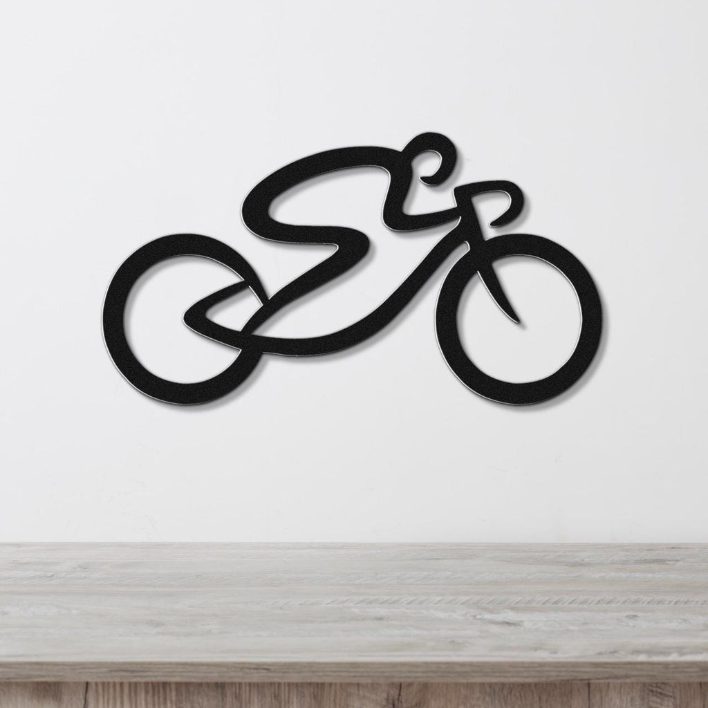 Black metal wall art in the shape of a stylized bicycle with flowing lines, mounted on a white wall above a light wood surface.