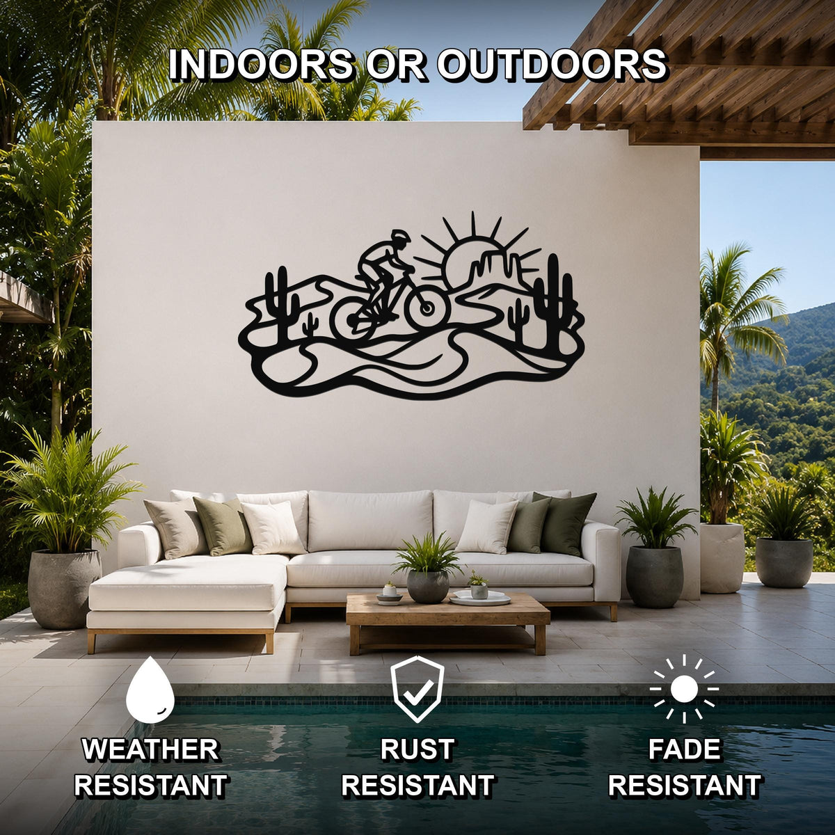 Black metal wall art featuring a desert silhouette of a cyclist, cacti, and a sun, mounted on a white wall above a sofa in a patio living area.