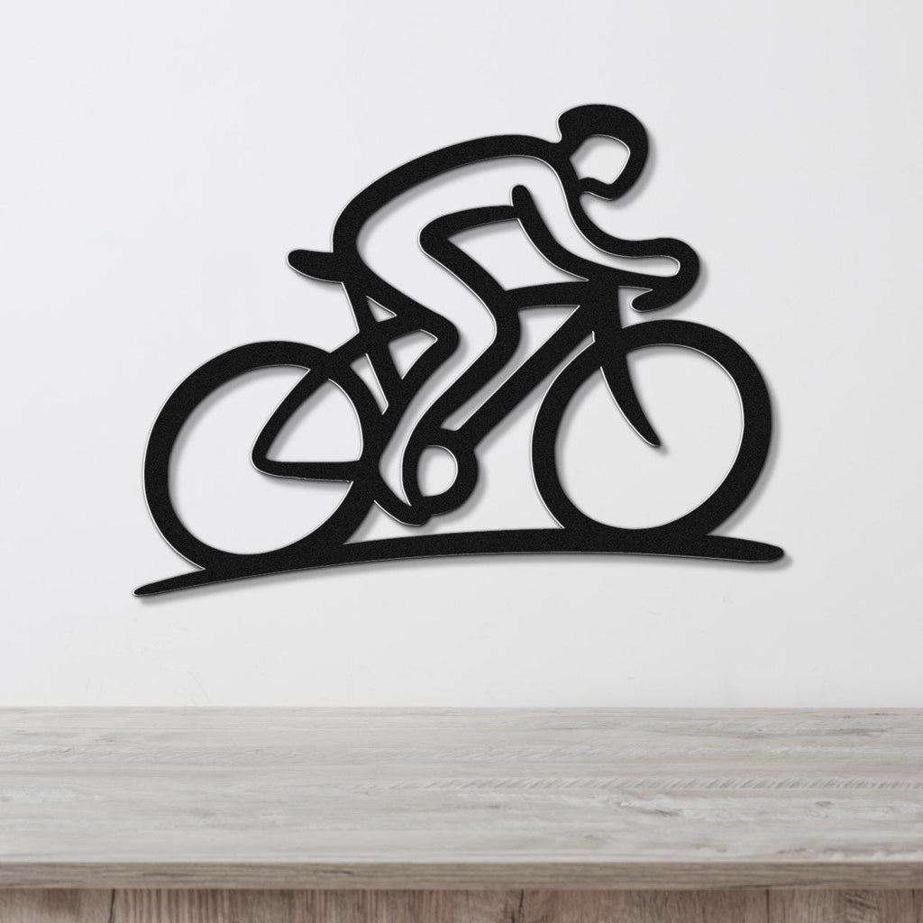 Black metal wall art featuring a dynamic cyclist silhouette with internal cutouts, mounted on a white wall above a wooden surface.