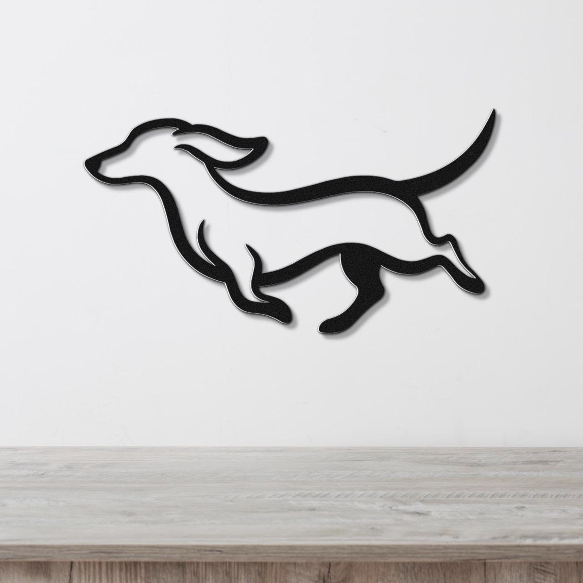 Black metal wall art in the silhouette of a running dachshund, mounted on a white wall above a light wood surface.