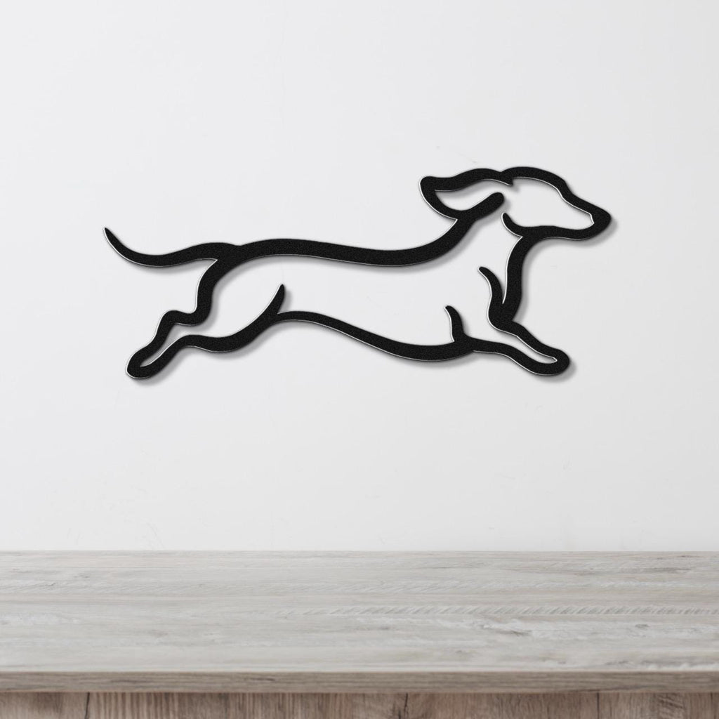 Black metal wall art of a dachshund in a running silhouette, mounted on a white wall above a light wood surface.
