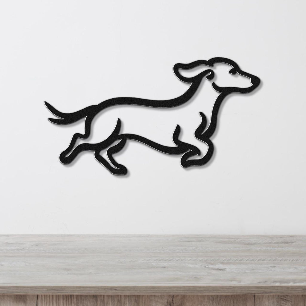 Black metal wall art in the silhouette of a running dachshund, mounted on a white wall above a light wood surface.