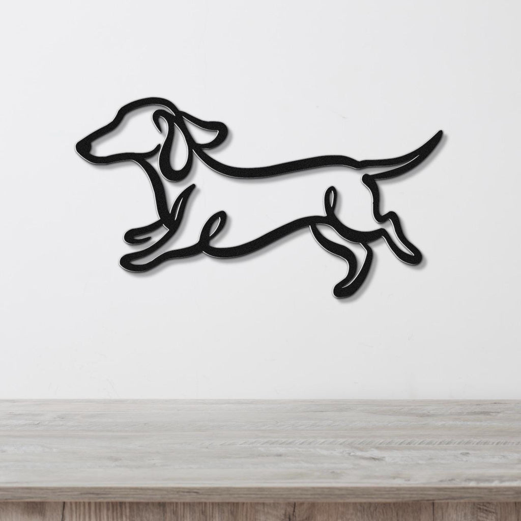 Black metal wall art of a dachshund in a running silhouette, mounted on a white wall above a light wood surface.