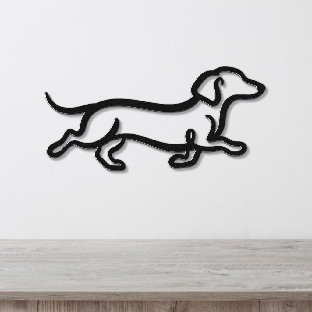 Black metal dachshund wall art in a running silhouette, mounted on a white wall above a light wood surface.