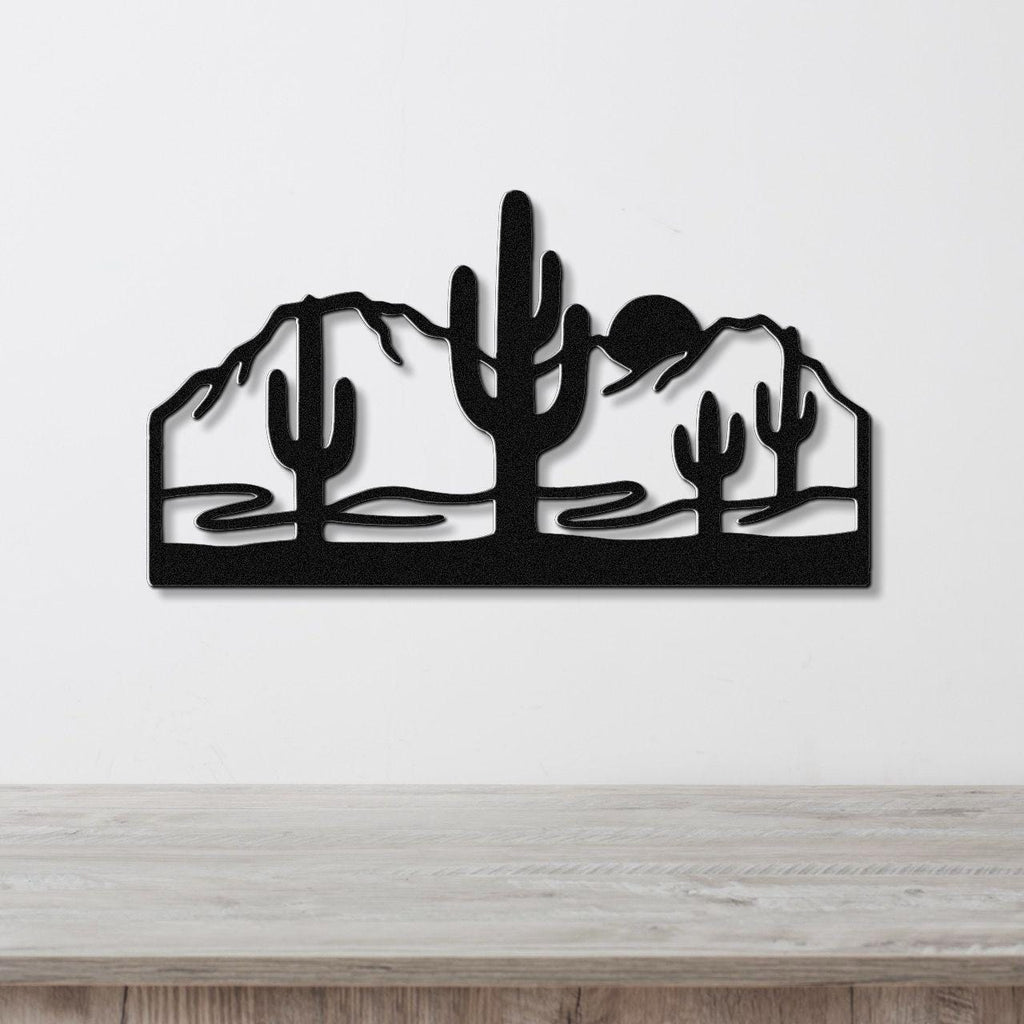 Black metal wall art with a desert silhouette of saguaro cacti and mountains, mounted on a white wall above a wooden counter.