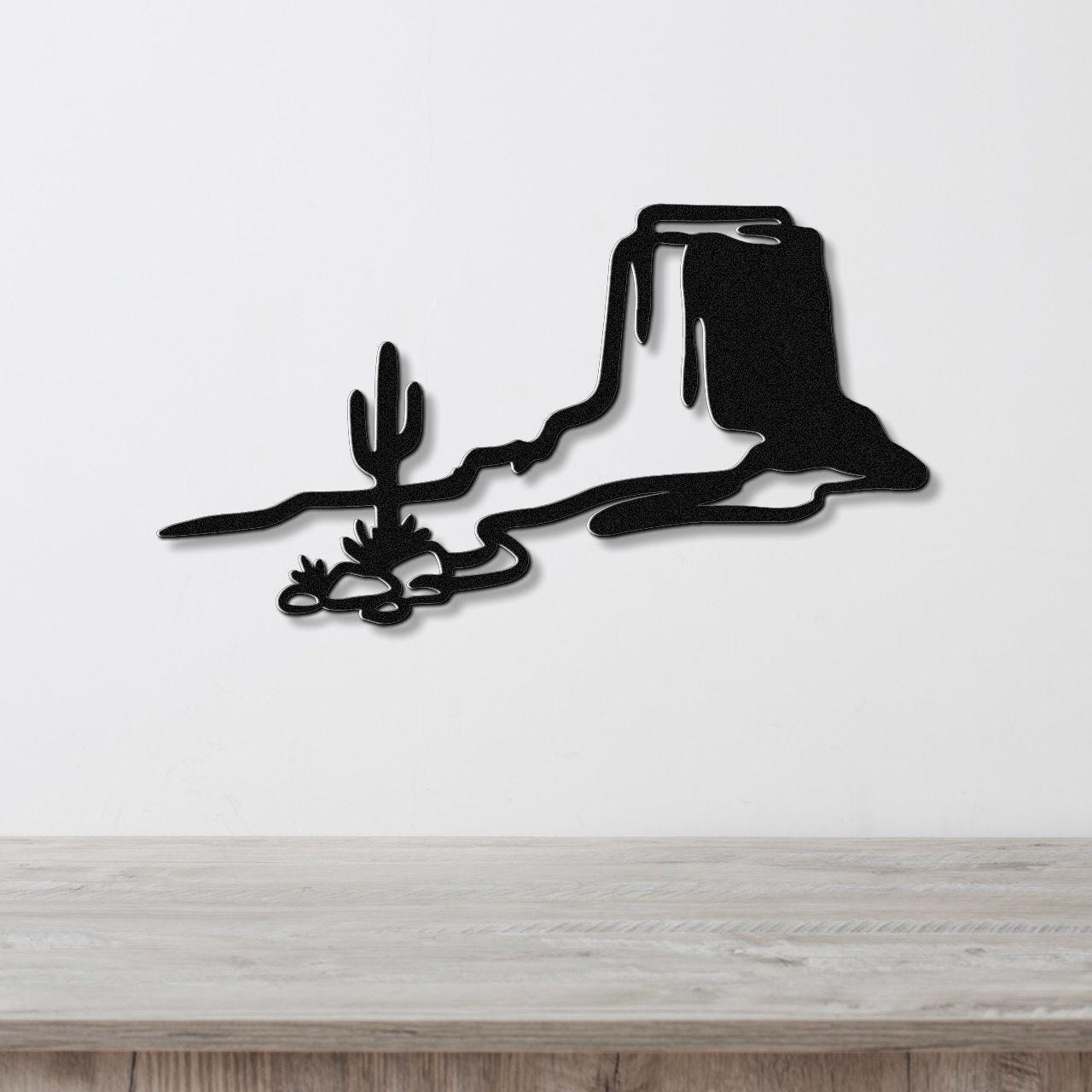 Black metal wall art featuring a desert silhouette with a saguaro cactus and mesa, mounted on a white wall above a wooden counter.