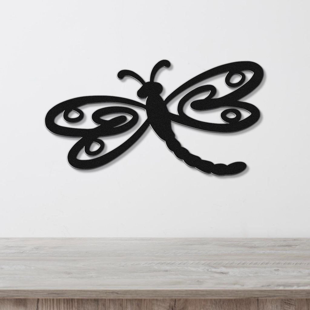 Black metal dragonfly wall art with intricate cutout wings, mounted on a white wall above a light wood surface.