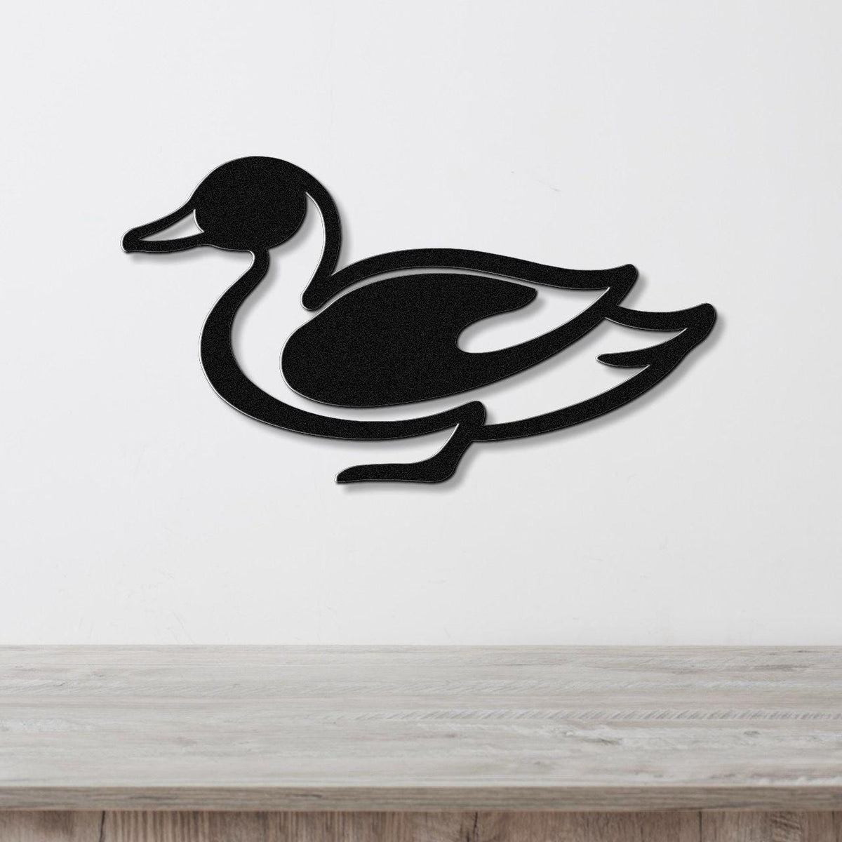 Black metal duck wall sculpture with a cutout silhouette design, mounted on a white wall above a light wood countertop.