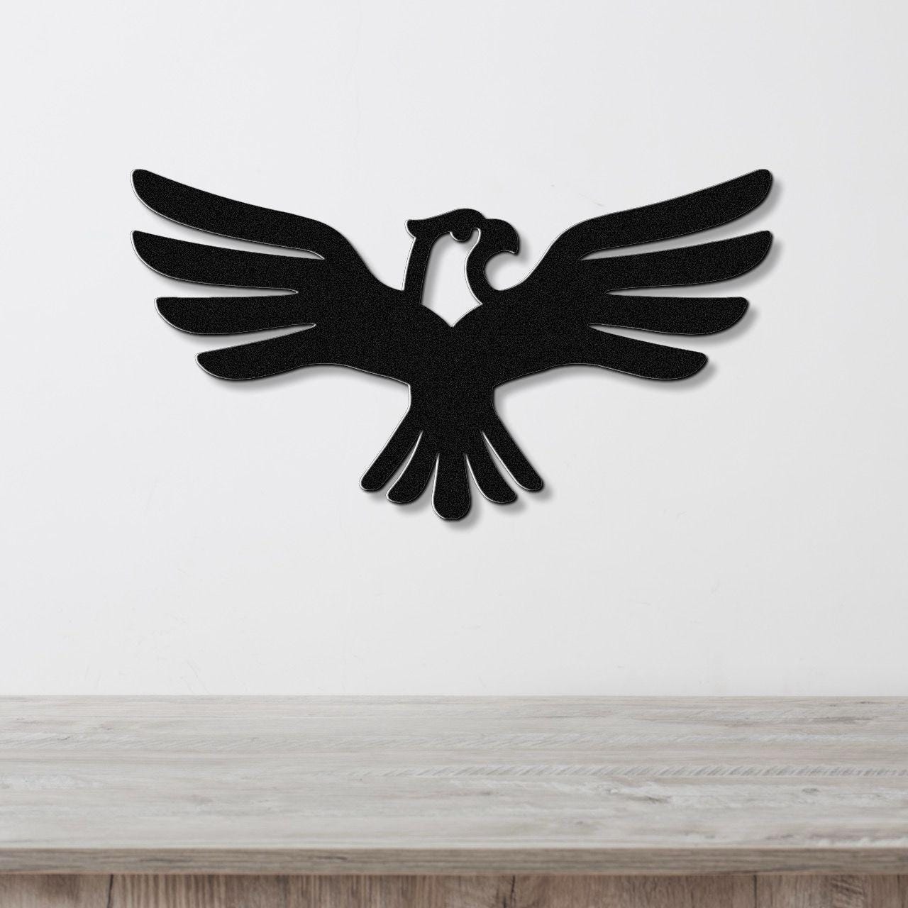 Black metal eagle wall art with outstretched wings and internal cutout details, mounted on a white wall above a light wood surface.